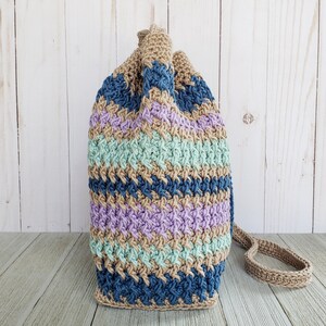 Pu&ograve; includere: Una borsa a cordoncino all'uncinetto con un motivo a righe in tonalit&agrave; di blu, verde, viola e marrone. La borsa ha una lunga tracolla in crochet marrone.