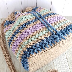 Pu&ograve; includere: Una borsa a mano all'uncinetto con un cinturino lungo. La borsa &egrave; realizzata con una variet&agrave; di colori, tra cui beige, blu, verde e viola.