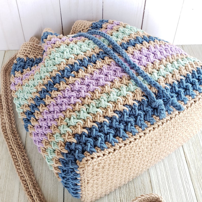 Pu&ograve; includere: Una borsa a mano all'uncinetto con un cinturino lungo. La borsa &egrave; realizzata con una variet&agrave; di colori, tra cui beige, blu, verde e viola.