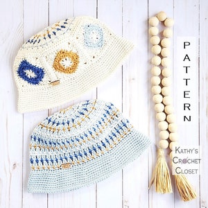 May include: Two crocheted bucket hats, one in white with blue and yellow accents, and one in light blue with yellow accents. The hats are on a white wooden surface with a wooden bead garland and a tassel.
