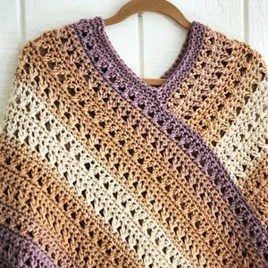 Puede incluir: Un poncho de ganchillo con escote en pico y un patr&oacute;n de punto calado. La prenda presenta un degradado de color en diagonal que transita por tonos crema, beige, marr&oacute;n claro y morado apagado en toda la superficie.