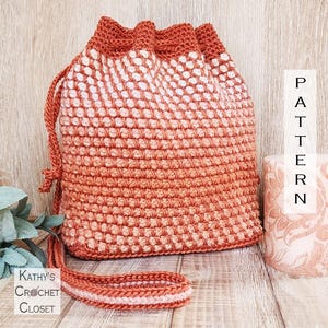May include: A handmade crochet drawstring bag in shades of orange and white. The bag features a textured stitch pattern and a matching strap. The words "PATTERN" and "Kathy's Crochet Closet" are visible in the image.
