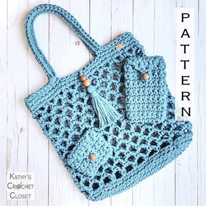 May include: A light blue crochet tote bag with two smaller matching pockets. The bag has a wooden bead and tassel detail. The tote bag is on a white wooden background with the word "PATTERN" written vertically in black.