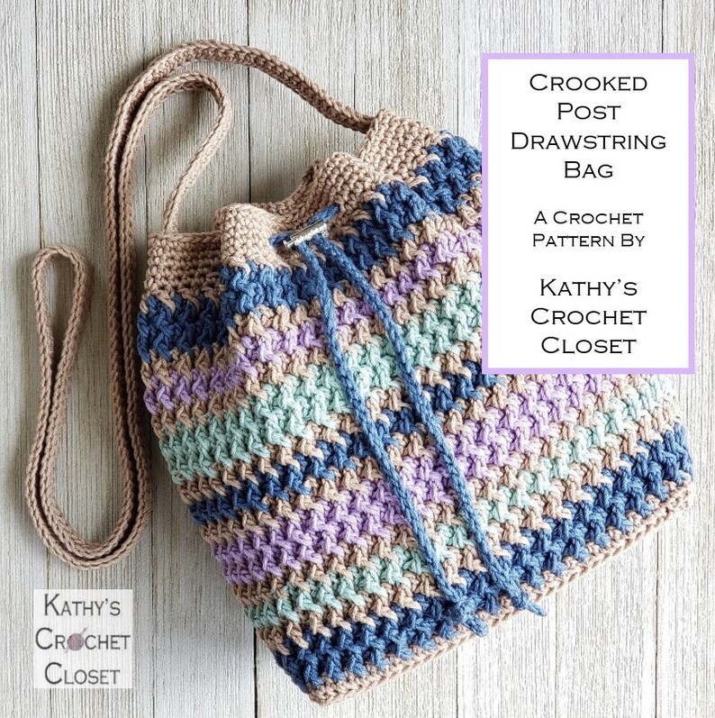 Pu&ograve; includere: Borsa a cordoncino all'uncinetto con un motivo a righe in tonalit&agrave; di blu, viola, verde e marrone. La borsa ha una tracolla lunga ed &egrave; realizzata con un punto all'uncinetto. Il testo "CROOKED POST DRAWSTRING BAG A CROCHET PATTERN BY KATHY'S CROCHET CLOSET" &egrave; in un riquadro viola sul lato destro dell'immagine.