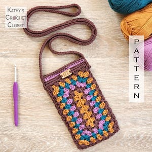 Puede incluir: Bolso de teléfono de ganchillo marrón con diseño de cuadrados de la abuela en turquesa, naranja y morado. Tiene una correa larga y el texto "Kathy's Crochet Closet". También se ven un ganchillo y ovillos de lana. El bolso mide unos 10 cm x 18 cm.