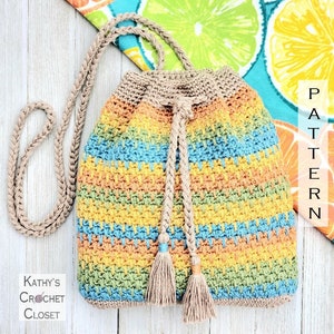 May include: A crocheted drawstring bag with a braided strap and tassels. The bag is made with a multi-coloured striped pattern in shades of blue, green, yellow, and orange. The bag is sitting on a wooden surface.