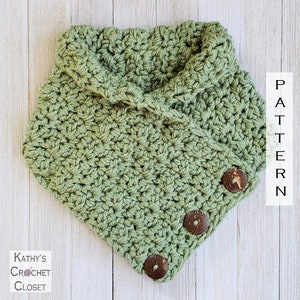 May include: A green crocheted cowl with a folded over collar and three wooden buttons. The cowl is on a white wood background.