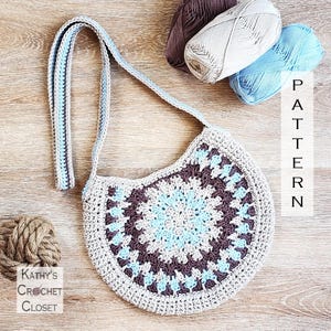 May include: A handmade crochet bag in a circular design with a long strap. The bag features a pattern of gray, brown, and light blue. The text "PATTERN" is visible on the right side of the image. The text "Kathy's Crochet Closet" is visible on the bottom left.