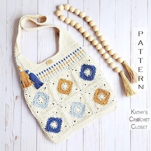 May include: A crocheted shoulder bag with a geometric pattern in shades of blue, yellow, and white. The bag has a long strap and tassels.