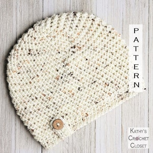 May include: A crocheted beanie hat in a cream color with flecks of brown and orange. The hat has a button on the side.