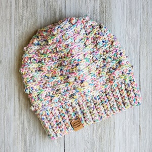 May include: A colorful crocheted hat with a multi-colored yarn. The hat has a textured design and a small brown tag that reads "Kathy's Crochet Closet".