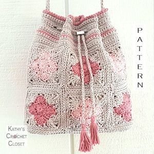 May include: A crocheted drawstring bag in a pink and beige colour scheme. The bag is made of granny squares with a floral design. The bag has a long strap and a tassel.