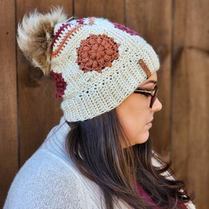 May include: A crocheted beanie with a pom pom, featuring a geometric pattern in shades of brown, cream, and burgundy. The beanie has a leather patch with the text "KCC" on it.
