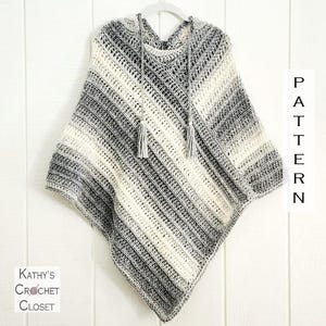 Puede incluir: Un poncho de ganchillo hecho a mano con un patrón de rayas blancas, grises y negras. El poncho tiene una capucha con borlas y se muestra en una percha. El texto "PATTERN" es visible en el lado derecho y "Kathy's Crochet Closet" en el izquierdo.