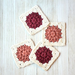 May include: Four crocheted squares with a white border and a red, pink, or orange center. The squares are made with a textured stitch.