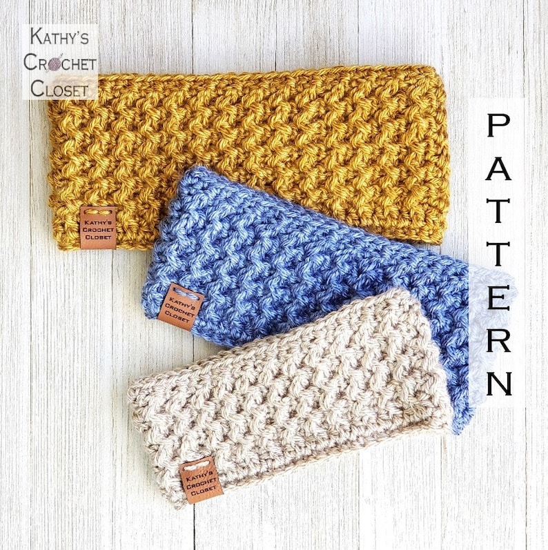 Op de afbeelding: Drie gehaakte hoofdbanden in verschillende kleuren: mosterdgeel, lichtblauw en beige. Elke hoofdband heeft een bruin lederen label met de tekst "Kathy's Crochet Closet".