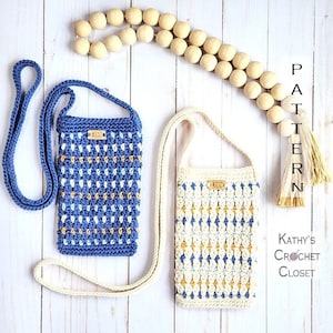 May include: Two crocheted crossbody bags with a blue and white pattern and a cream and white pattern. The bags have a small wooden tag with the letters "KCC" on them. The bags are on a white wooden background with a wooden bead garland.