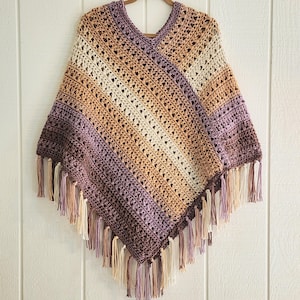 Puede incluir: Un poncho de ganchillo con cuello en V que presenta un patr&oacute;n de rayas diagonales en tonos morado, tostado, crema y marr&oacute;n. La prenda est&aacute; confeccionada con un dise&ntilde;o de punto abierto y rematada con largos flecos multicolores en el borde.