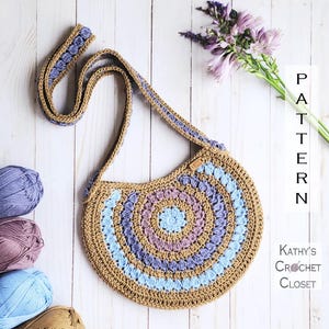 Puede incluir: Bolso redondo de ganchillo hecho a mano en tonos beige, azul y morado. El bolso presenta una correa larga y un diseño en espiral. El texto "PATTERN" y "Kathy's Crochet Closet" son visibles. Ovillos de lana y flores en el fondo.