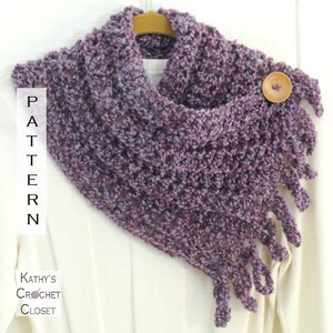 May include: Purple crochet cowl with a fringe and a wooden button. The cowl is hanging on a wooden hanger. The text "PATTERN" is visible on the left side of the image. The text "Kathy's Crochet Closet" is visible on the bottom left side of the image.