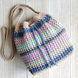 Pu&ograve; includere: Una borsa a cordoncino all'uncinetto con una lunga tracolla. La borsa &egrave; realizzata con una variet&agrave; di colori, tra cui marrone, blu, viola e verde.