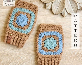 May include: Two crocheted fingerless gloves. The gloves are brown with a square design in the center featuring light blue and a central flower design. The text "Kathy's Crochet Closet" is in the upper left corner. A leather tag with "KCC" is attached.