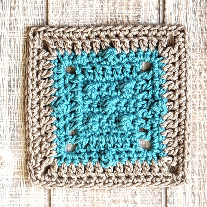 Puede incluir: Un cuadrado tejido a crochet con un centro turquesa y un borde marr&oacute;n. El cuadrado est&aacute; hecho con un patr&oacute;n de punto de abuela.
