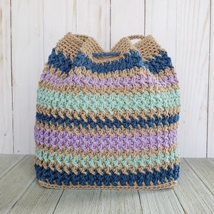 Pu&ograve; includere: Una borsa a mano all'uncinetto con un motivo a righe in tonalit&agrave; di blu, verde, viola e marrone. La borsa &egrave; realizzata con un filato testurizzato e ha una chiusura con coulisse.