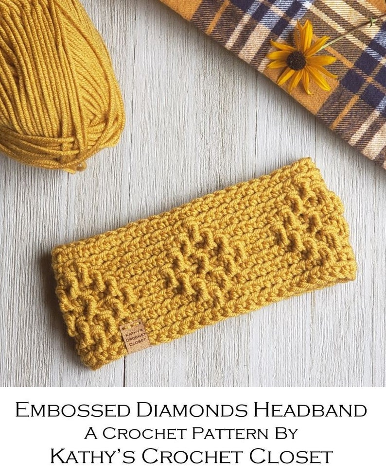 Op de afbeelding: Een gele gehaakte hoofdband met een ruitpatroon. De hoofdband ligt op een licht houten oppervlak met een bolletje gele garen en een geruite stof op de achtergrond. De tekst "Kathy's Crochet Closet" staat op een bruin label dat aan de hoofdband is bevestigd.