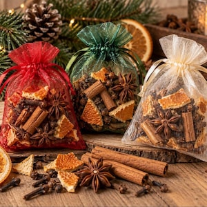 May include: Three sheer organza drawstring bags in red, green, and cream, each filled with a potpourri mix of dried orange slices, whole star anise, cinnamon sticks, and cloves, with loose spices scattered on the wooden surface.