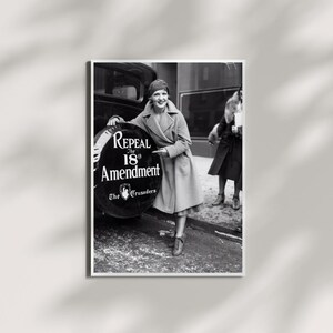 May include: A black and white photograph showing a person in a long coat leaning against a vehicle spare tire cover. The cover features the text Repeal The 18th Amendment and The Crusaders. Another person stands in the background wearing a dark coat.