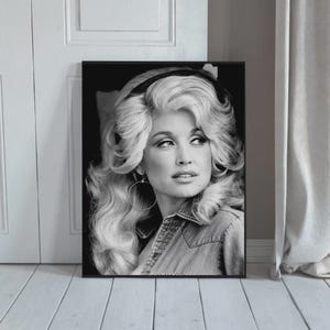 May include: A black and white portrait print featuring a person with voluminous, wavy blonde hair styled with a dark headband. The subject is wearing a collared shirt and large hoop earrings, looking toward the right side of the frame.