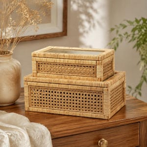 May include: Two rectangular storage boxes stacked on top of each other, crafted from light brown woven rattan with a natural finish. The boxes feature a grid-patterned cane webbing on the sides and a clear glass panel on the top lid.