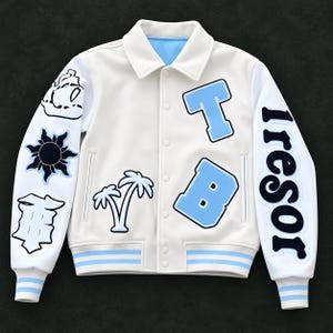 Può includere: Una giacca varsity bianca con dettagli azzurri, colletto e chiusura con bottoni a pressione. Il davanti presenta le lettere T e B in azzurro e un disegno di palma. Le maniche mostrano una nave, un sole e la parola tresor in nero.