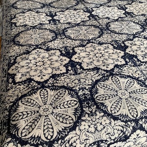 May include: A navy blue and cream-colored floral patterned bedspread. The bedspread features large, stylized floral designs and smaller floral and leaf patterns. The color scheme is a classic combination, creating a visually appealing textile for a bedroom.