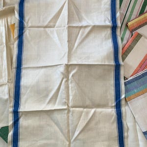 May include: Cream-colored linen kitchen towel with a blue stripe border. Several other striped towels in various colors are visible in the background. The main towel is folded and has visible creases.