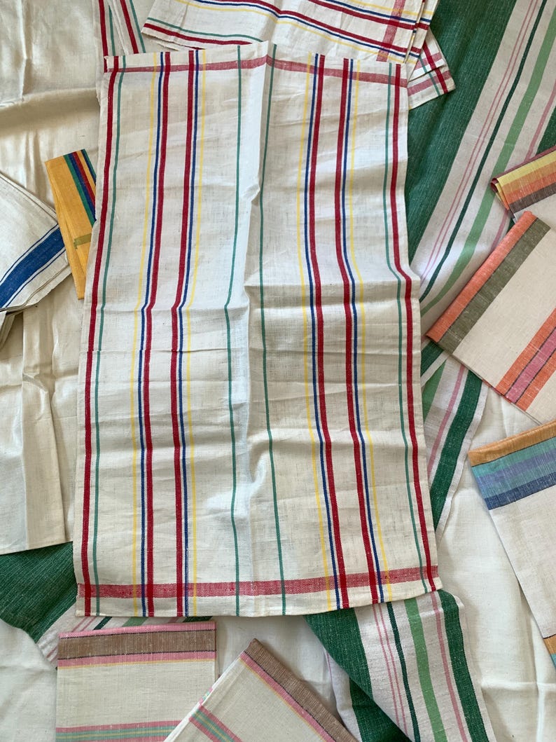 May include: White linen kitchen towels with vertical stripes in red, blue, yellow, and green. Several other striped towels are visible, with various stripe colors and patterns. The towels are likely for kitchen or home use.
