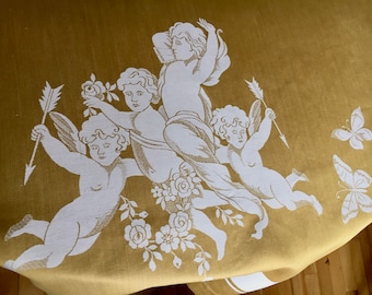 May include: Mustard yellow tablecloth with a white cherub and butterfly design. The cherubs are depicted with wings, holding arrows and roses. The tablecloth has a decorative border.