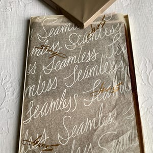 May include: A brown box with the brand name "Hanes" in a cursive font. Inside, the box contains a pair of seamless stockings, wrapped in tissue paper printed with the word "Seamless" in a repeating pattern. The Hanes logo is also printed on the tissue paper.