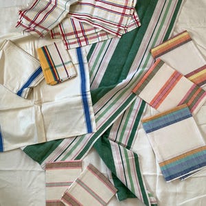 May include: A collection of assorted vintage linen napkins and cloths. The napkins feature various striped and plaid patterns in colors like red, green, blue, yellow, and pink. The linens are arranged on a white surface.