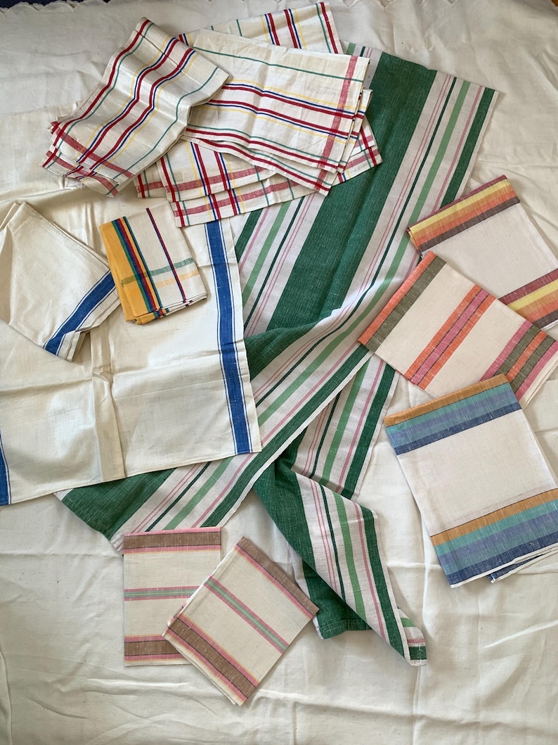 May include: A collection of assorted vintage linen napkins and cloths. The napkins feature various striped and plaid patterns in colors like red, green, blue, yellow, and pink. The linens are arranged on a white surface.