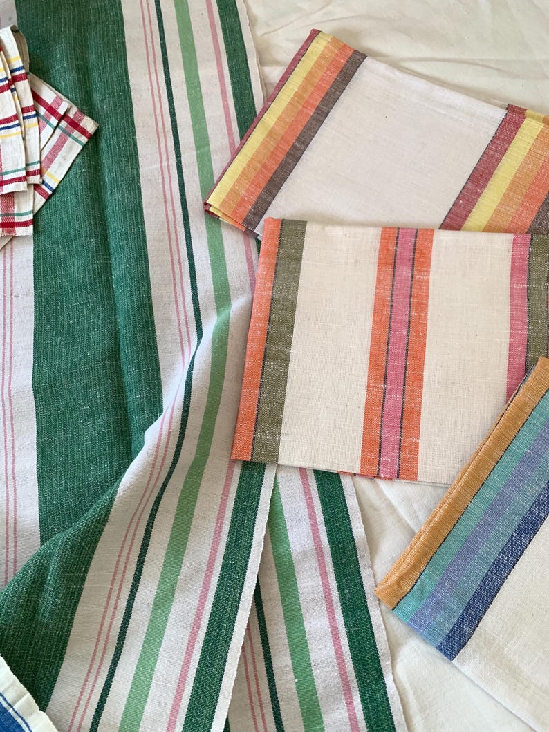 May include: Assortment of striped fabric items in various colors. Includes green, pink, and white striped fabric, along with several rectangular pieces featuring stripes in orange, yellow, and blue. The textiles appear to be linen or a similar natural fiber.