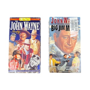 Può includere: Due videocassette VHS con John Wayne. La copertina sinistra è intitolata The John Wayne Story con diverse immagini dell'attore in vari ruoli. La copertina destra è intitolata John Wayne is Big Jim McLain con un grande ritratto.