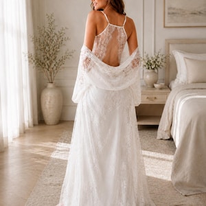 May include: A white floor-length lace robe and matching slip dress set. The slip dress features thin spaghetti straps and an open back design. The robe has long, loose sleeves and is crafted from intricate floral lace fabric that drapes to the floor.