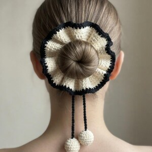 Può includere: Un elastico per capelli all'uncinetto color crema con un bordo arricciato rifinito in nero. L'accessorio presenta due sottili cordini neri all'uncinetto che pendono, terminando ciascuno con una piccola sfera o pon-pon all'uncinetto color crema.