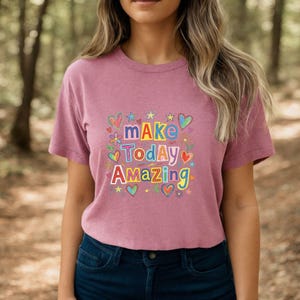 May include: A mauve short-sleeved t-shirt featuring a colorful graphic print with the text "MAKE TODAY AMAZING" in varied fonts and colors. The design is surrounded by small illustrations of hearts, stars, and flowers in blue, yellow, and red.