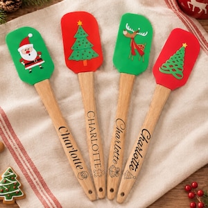 May include: Four silicone spatulas with wooden handles, each personalized with the name Charlotte. The spatulas feature festive designs including Santa Claus, a Christmas tree, a reindeer, and a stylized tree, all in red and green colors.
