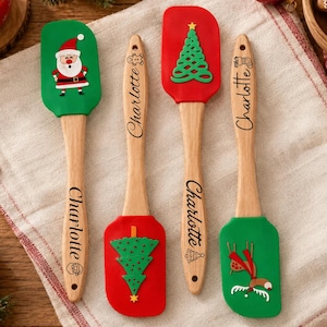 May include: Four kitchen spatulas with wooden handles personalized with the name Charlotte. Two spatulas have green silicone heads featuring a Santa Claus and a reindeer. Two spatulas have red silicone heads featuring a Christmas tree.