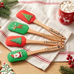 May include: Four silicone spatulas with wooden handles, each personalized with the name Charlotte. The spatulas feature festive designs including a green Christmas tree, a reindeer, a patterned tree, and a Santa Claus on red and green heads.