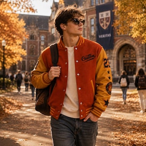 Könnte beinhalten: Eine Collegejacke mit rostorangem Rumpf und senfgelben Ärmeln, einem cremefarbenen Rundhals-Shirt und einer dunkelgrauen Jeans. Die Jacke hat silberne Druckknöpfe, das Wort Custom in schwarzer Schreibschrift und Aufnäher, darunter die Zahl 23.
